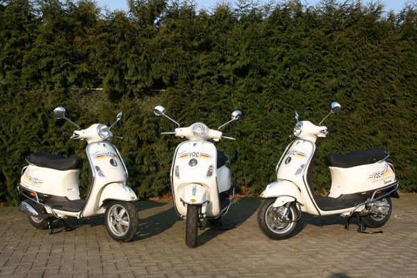 Op de stoep staan drie scooters van rijschool van Oijen waarop kandidaten gaan lessen op hun scooterrijbewijs te halen.